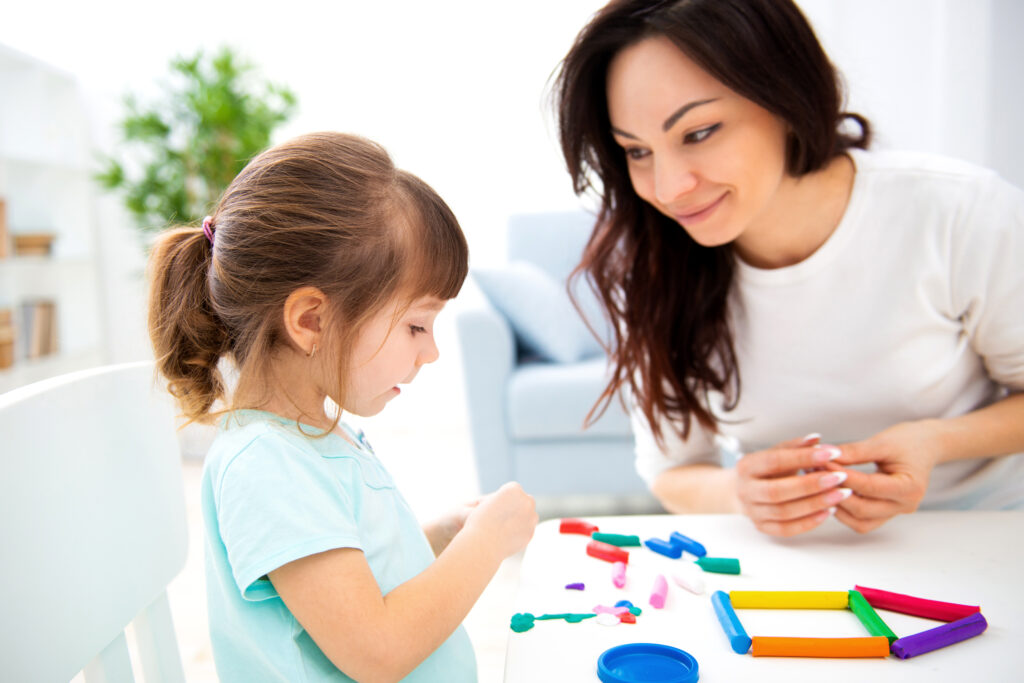 Home-Based vs. Clinic-Based ABA Therapy in Atlanta. Mom and little daughter sculpt new house of plasticine. Child development and education. Family leisure with a child. Happy childhood.