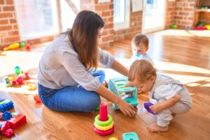 Beautiful Board Certified Behavior Analyst (BCBA) and toddlers playing around lots of toys at kindergarten