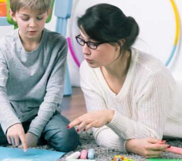 A young child with autism sitting with a therapist, engaging in communication activities in a supportive, educational setting.