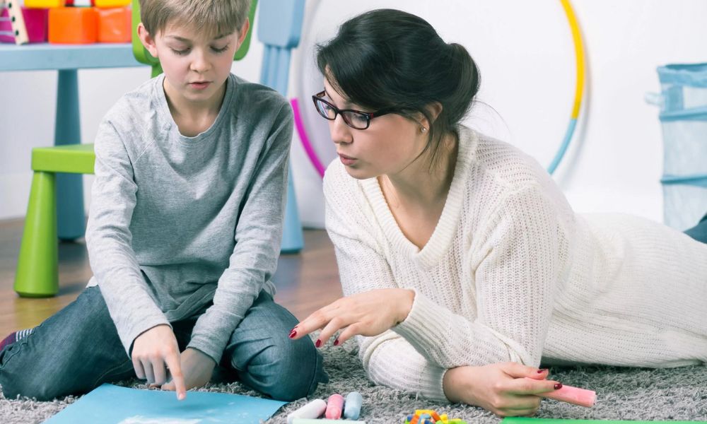 A young child with autism sitting with a therapist, engaging in communication activities in a supportive, educational setting.