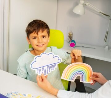 An occupational therapist guiding a child in balancing on a therapy ball while practicing hand–eye coordination and motor skills in a bright, organized therapy room.